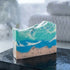 Bar of soap with blue and green design on a black surface, blurred background